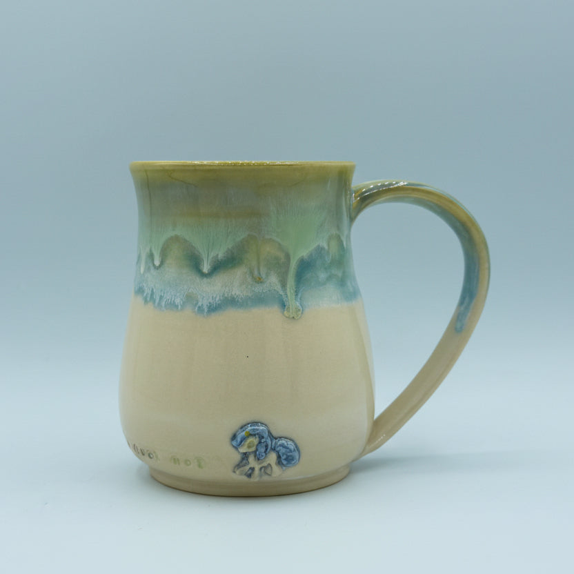 Ceramic mug with green and beige gradient and a blue logo on a white background