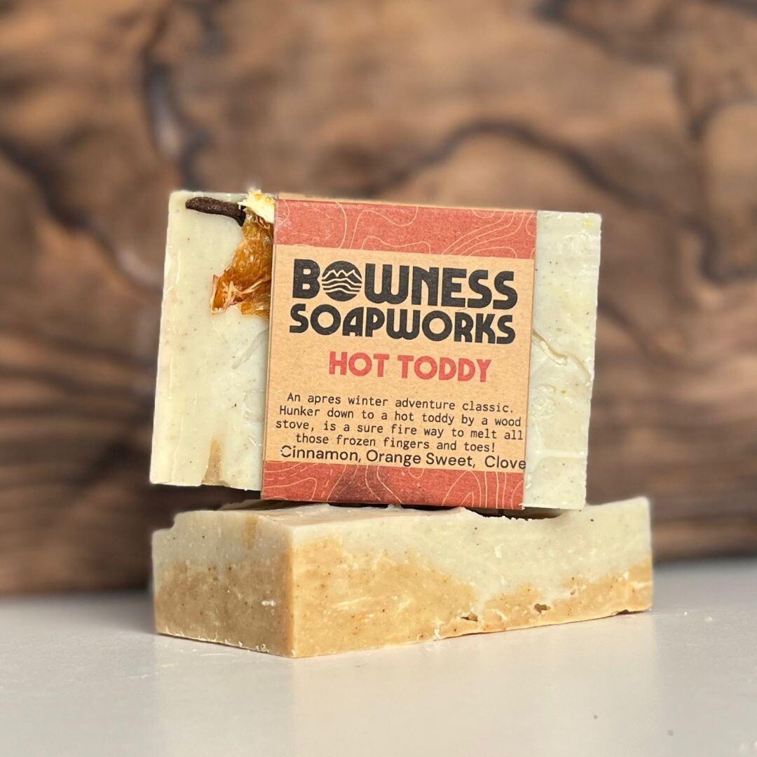 Hot Toddy soap by Bowness Soapworks in Calgary, stacked with cinnamon, orange, and clove ingredients visible on a wood-toned background