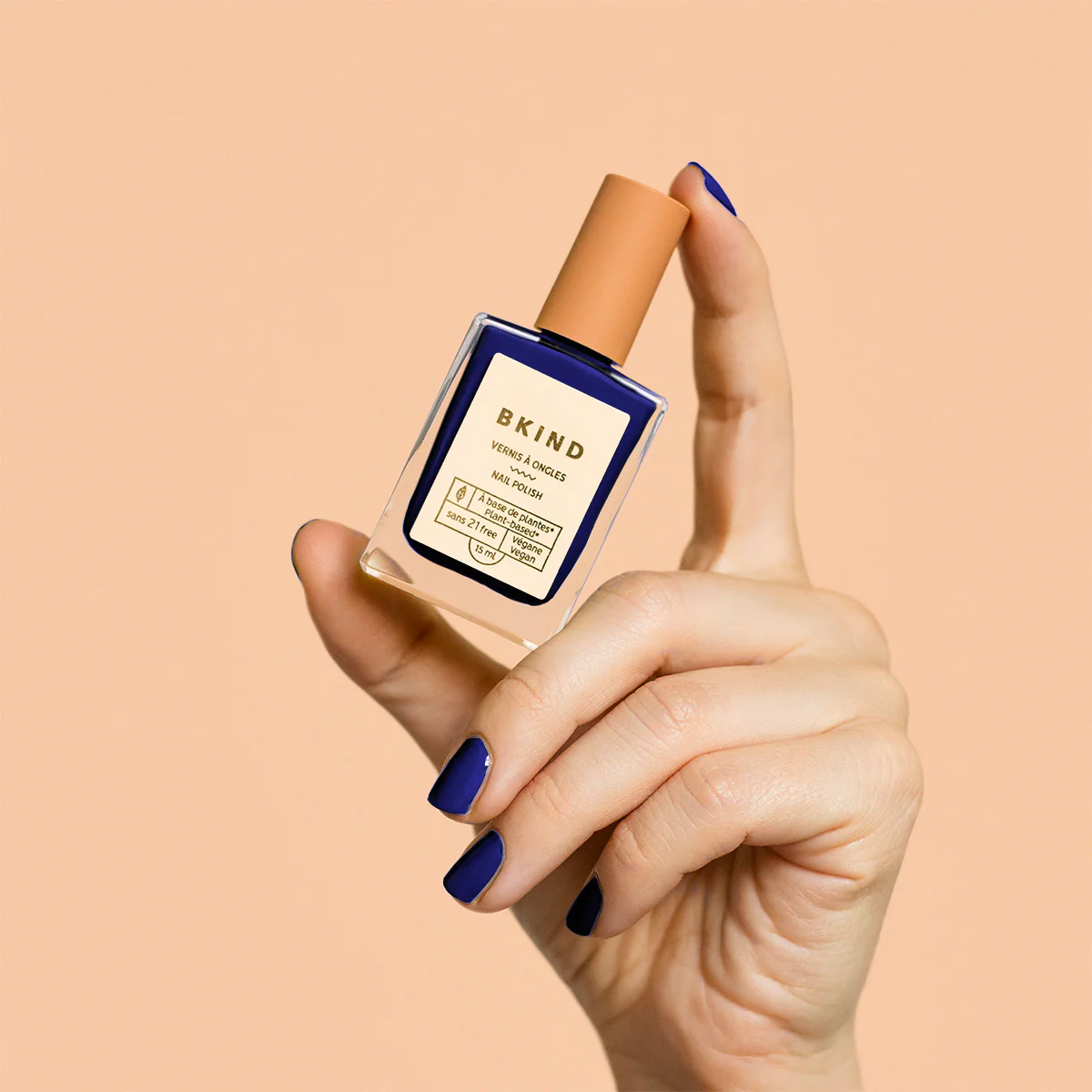 Hand holding BKIND On The Rocks nail polish with matching navy nails