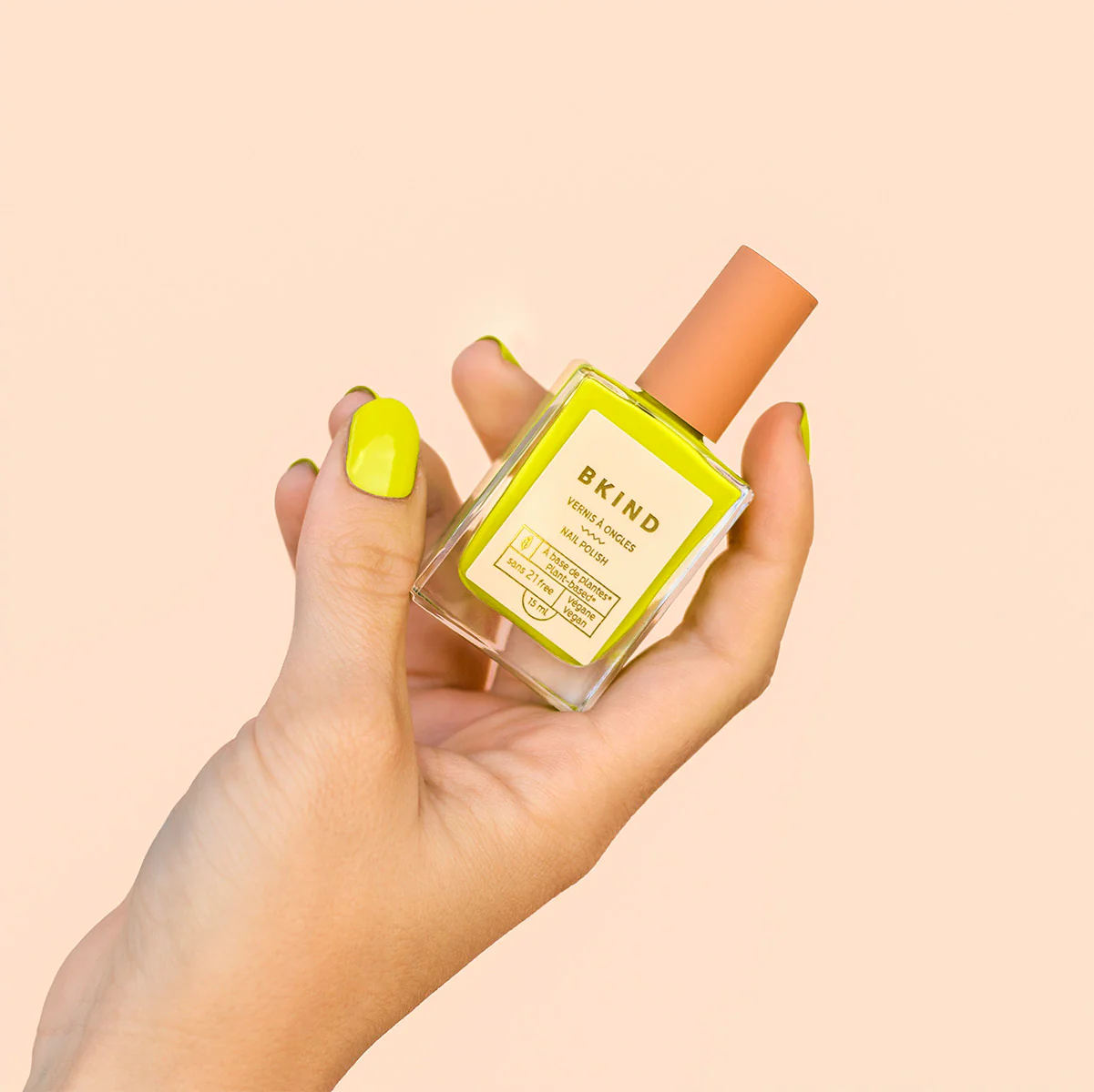 Hand holding BKIND Wild nail polish bottle with matching yellow nails