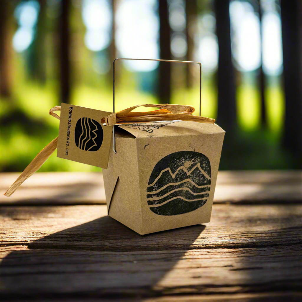 Kraft take-out box gift set by Bowness Soapworks, stamped with mountain logo and styled on a rustic wood table outdoors