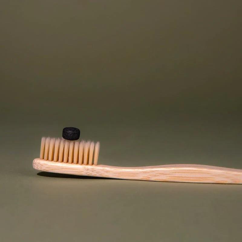Charcoal toothpaste tab resting on bamboo toothbrush – Calgary zero-waste dental routine