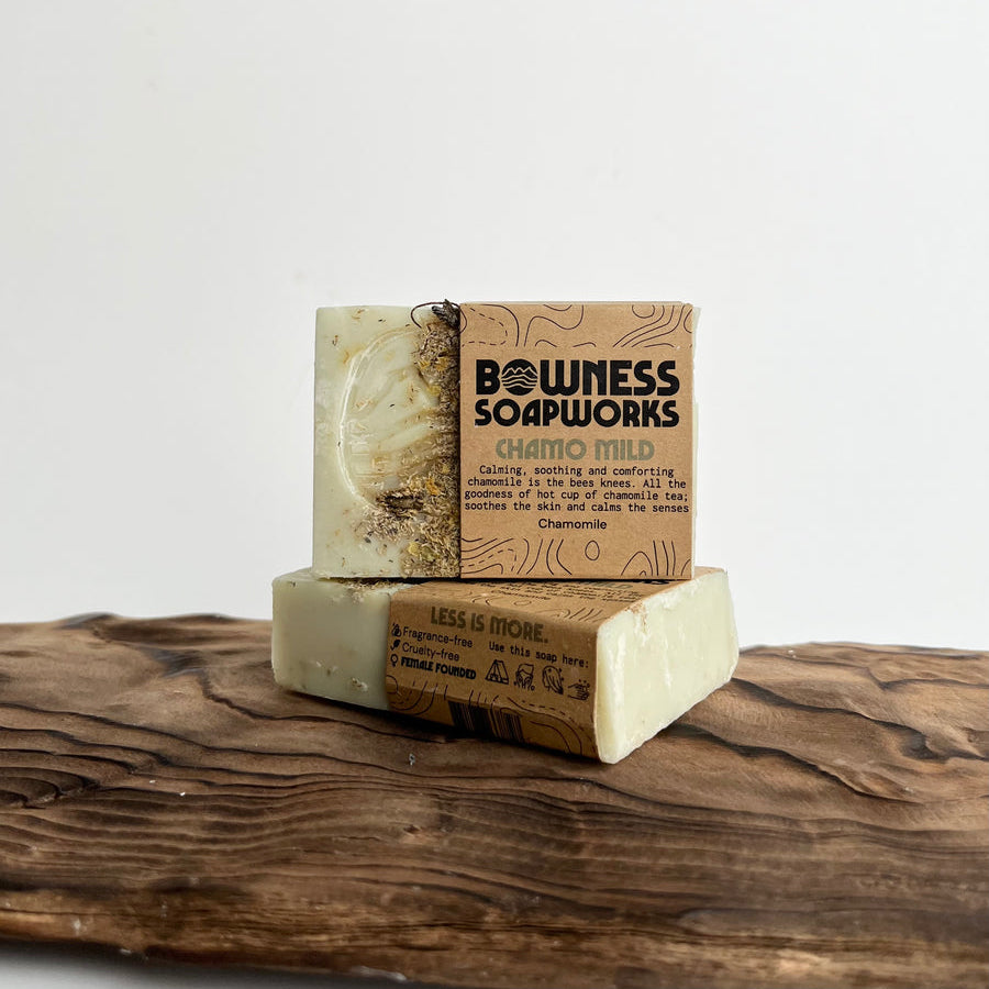 Stacked chamomile soap bars made in Calgary by Bowness Soapworks, shown on carved wood with visible dried botanicals and kraft paper wrap