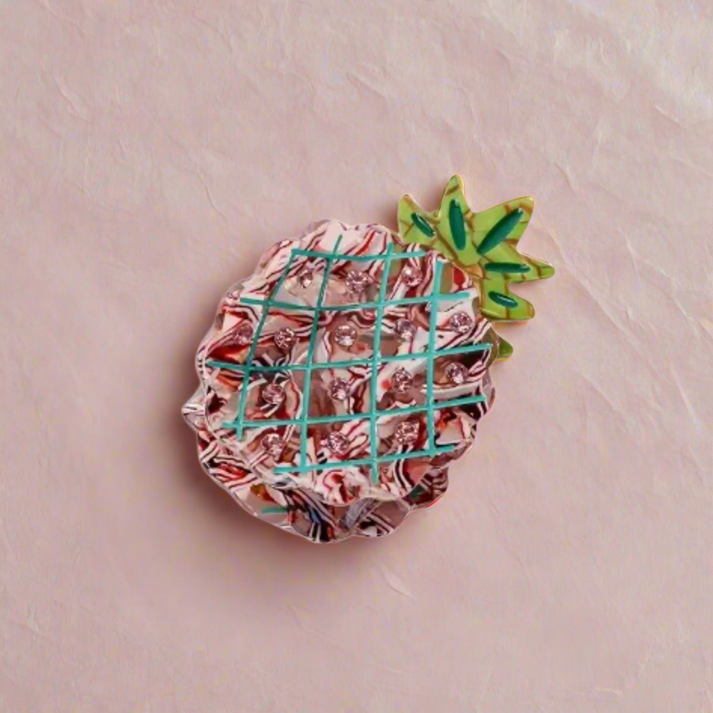 Pineapple-shaped pink acetate hair clip on textured blush background – Calgary hair accessories for bold summer style.