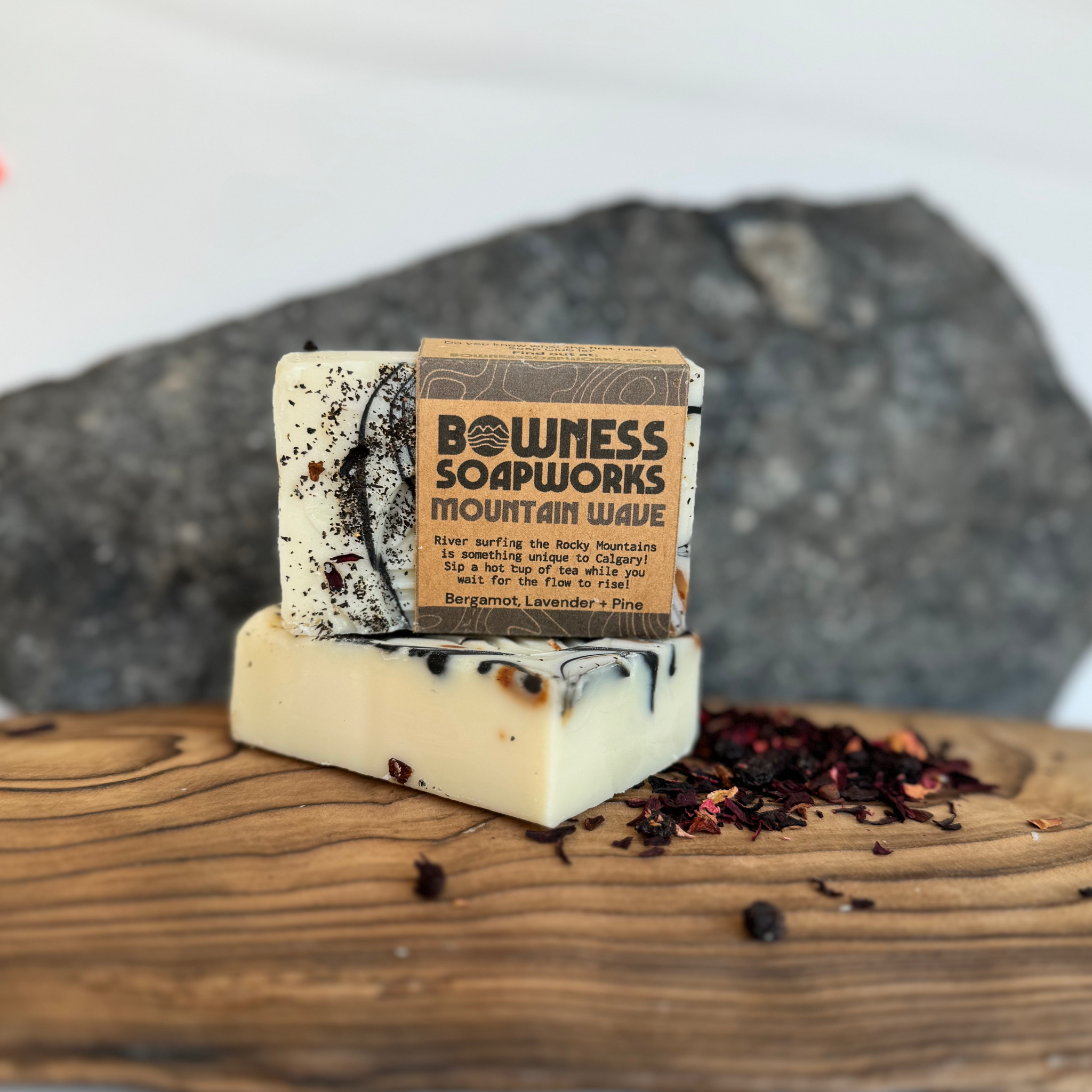 Stacked Mountain Wave soap bars made in Calgary by Bowness Soapworks, with lavender and pine ingredients shown on wood in front of stone