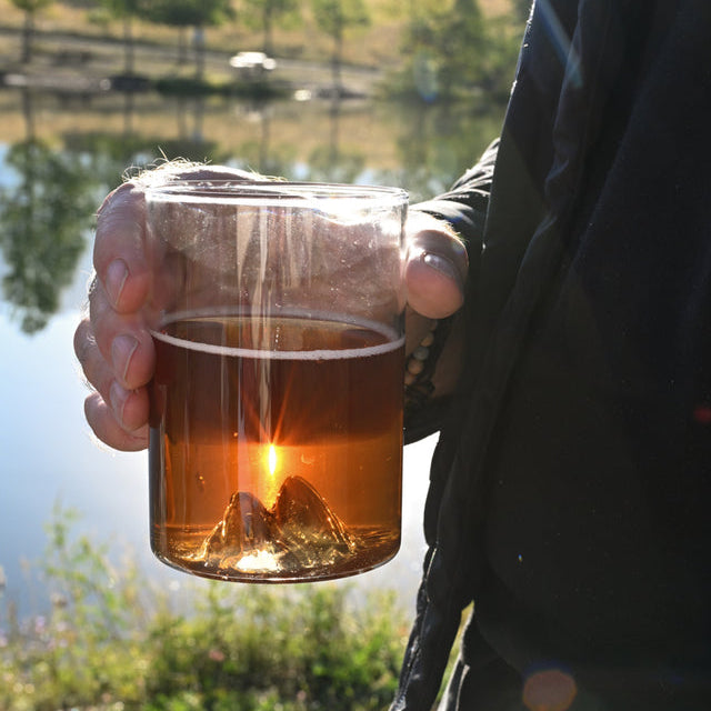 Two Lions MTNPK pint glass held outdoors with amber drink and sunset glow, available at Greenbriar Market in Calgary