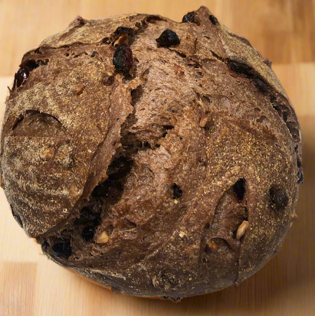 Close-up of Noir Sourdough bread with dark chocolate, cranberries, and walnuts on a wooden board, baked fresh at Greenbriar Market in Calgary