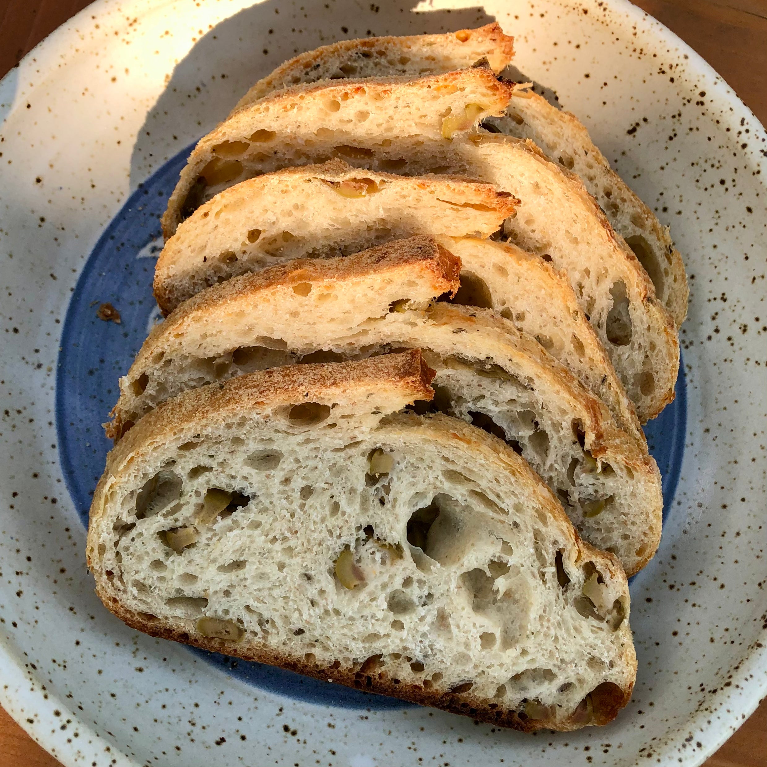 Slices of olive and asiago sourdough bread from Calgary’s Homestead Bakery on a handmade speckled ceramic plate