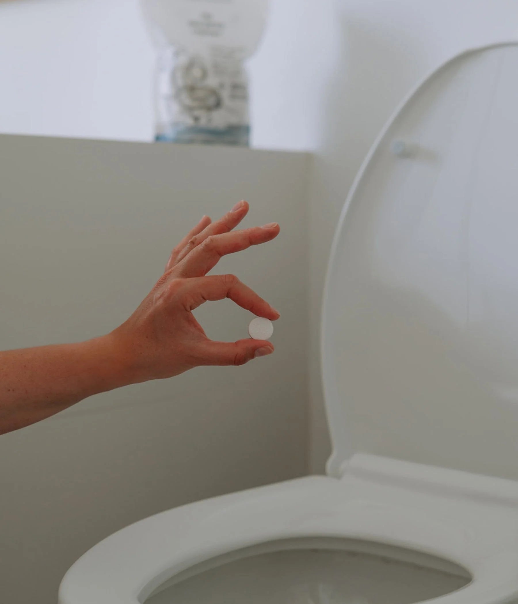 Hand holding an unscented toilet bowl cleaner tablet above a toilet, biodegradable refill tab sold individually at a Calgary refill bar