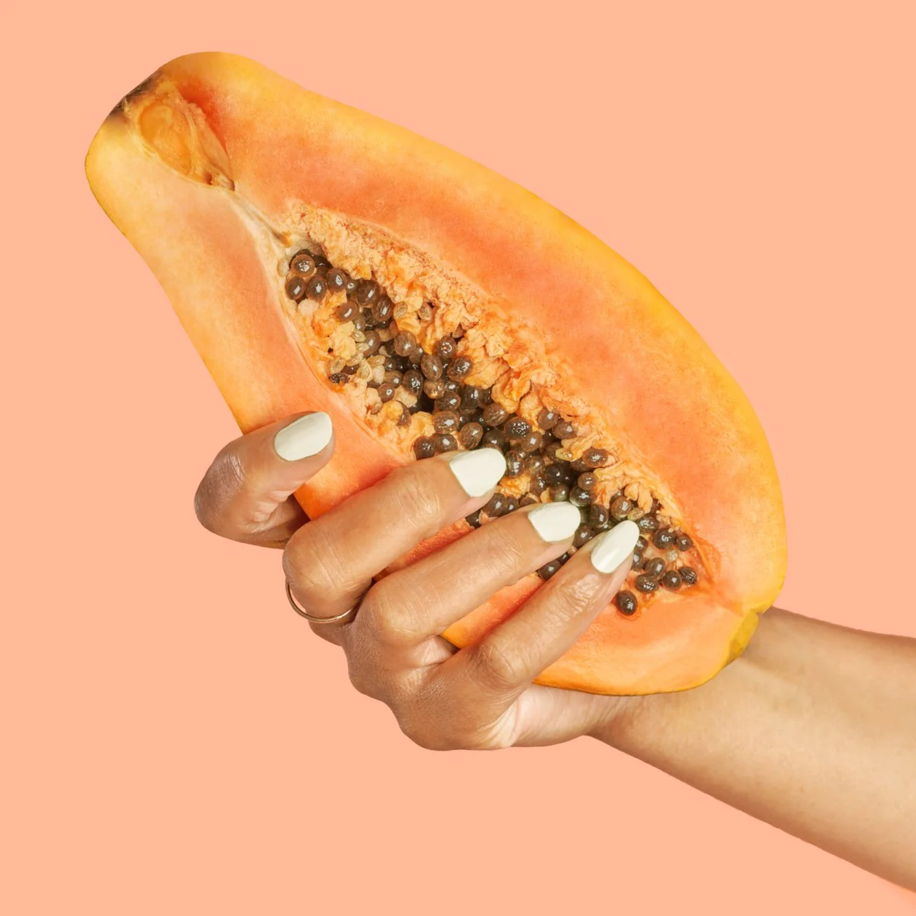 Hand with BKIND Bichon white nail polish holding papaya – vegan manicure available in Calgary.