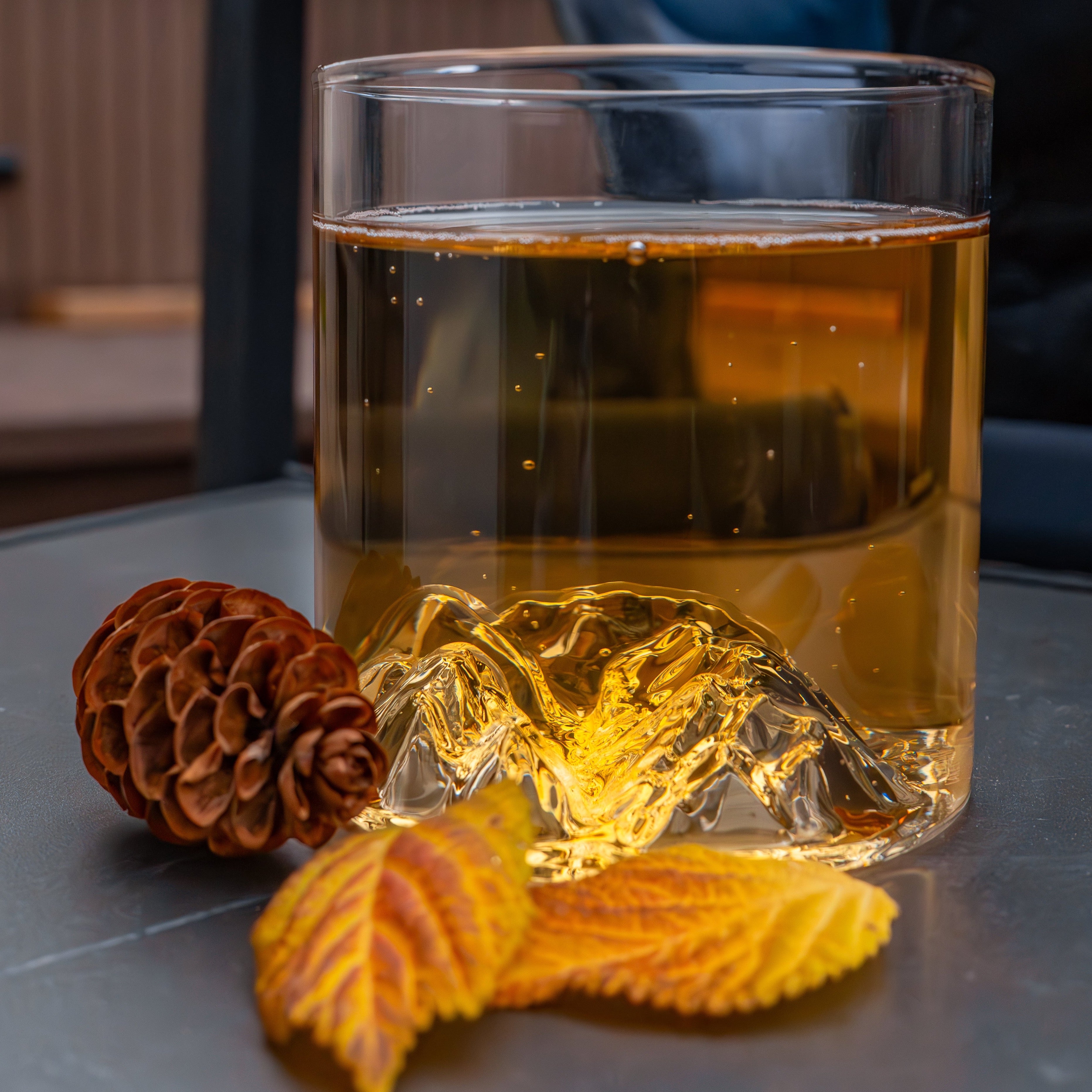 Lake Louise tumbler glass with 3D mountain detail on patio table, styled with pinecone and autumn leaves