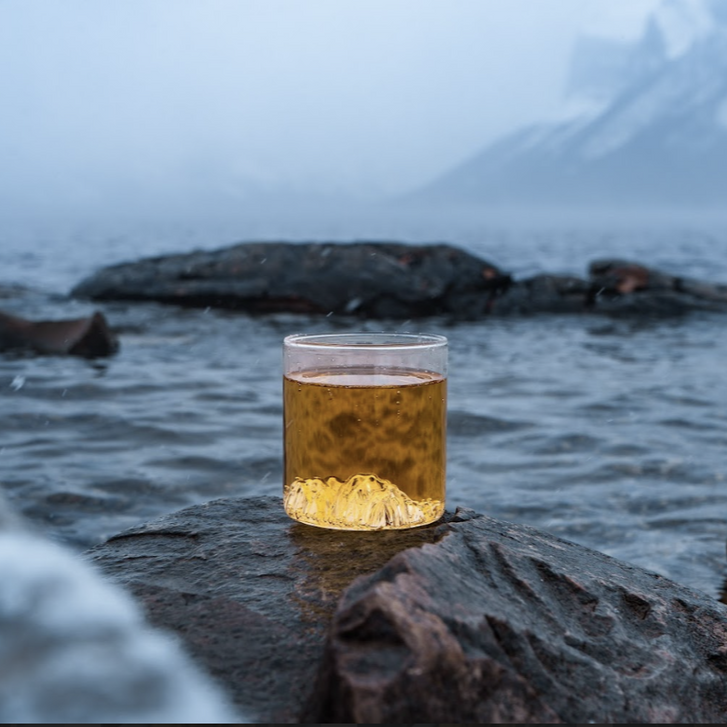 MTNPK Lake Minnewanka tumbler glass on wet rock with lake backdrop, available at Greenbriar Market Calgary