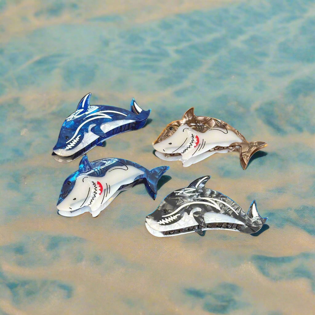 Four Lola shark-shaped claw clips on a sandy beach background