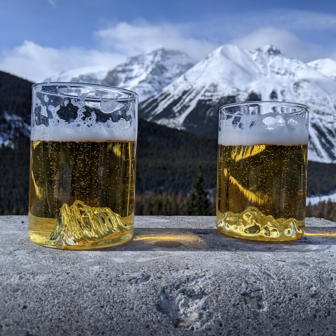 Mountain pint glasses with 3D reliefs of Mt. Rundle and Mt. Edith Cavell filled with beer on snowy backdrop | photographed outdoors