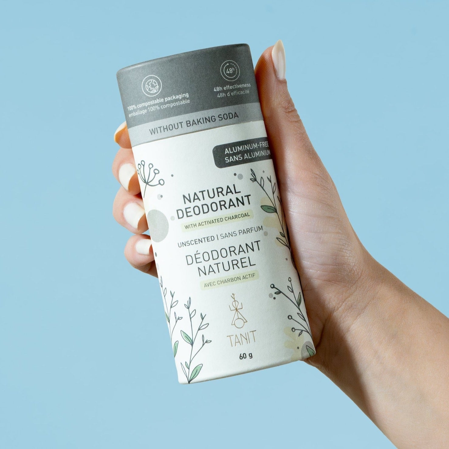 Hand holding Tanit natural deodorant tube with charcoal label against a pastel blue background – Calgary low waste personal care