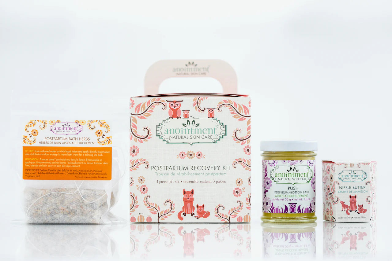 Postpartum recovery kit contents including herbal bath herbs, nipple butter, and perineum balm arranged together for new mom care