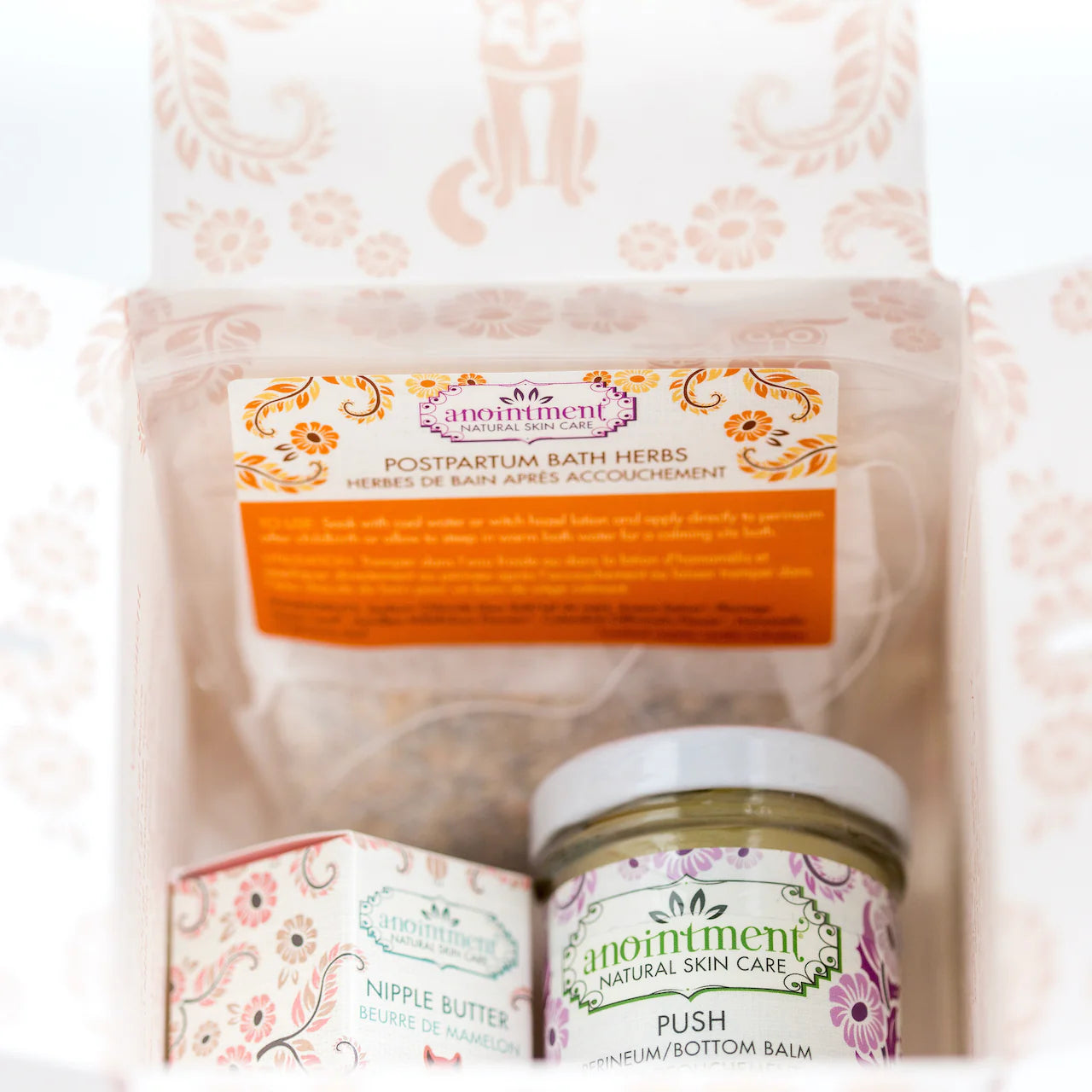 Open postpartum recovery kit showing herbal bath herbs, nipple butter, and perineum balm packaged for new moms