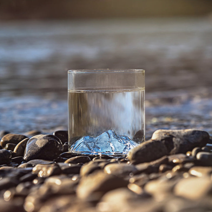 Glass tumbler featuring Pyramid Mountain design, placed on smooth river rocks with water in the background