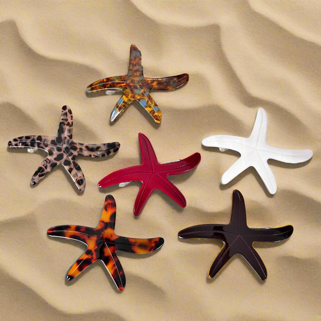 Six Sebeana starfish hair barrettes on textured beach sand – sustainable Calgary hair accessories made from cellulose acetate
