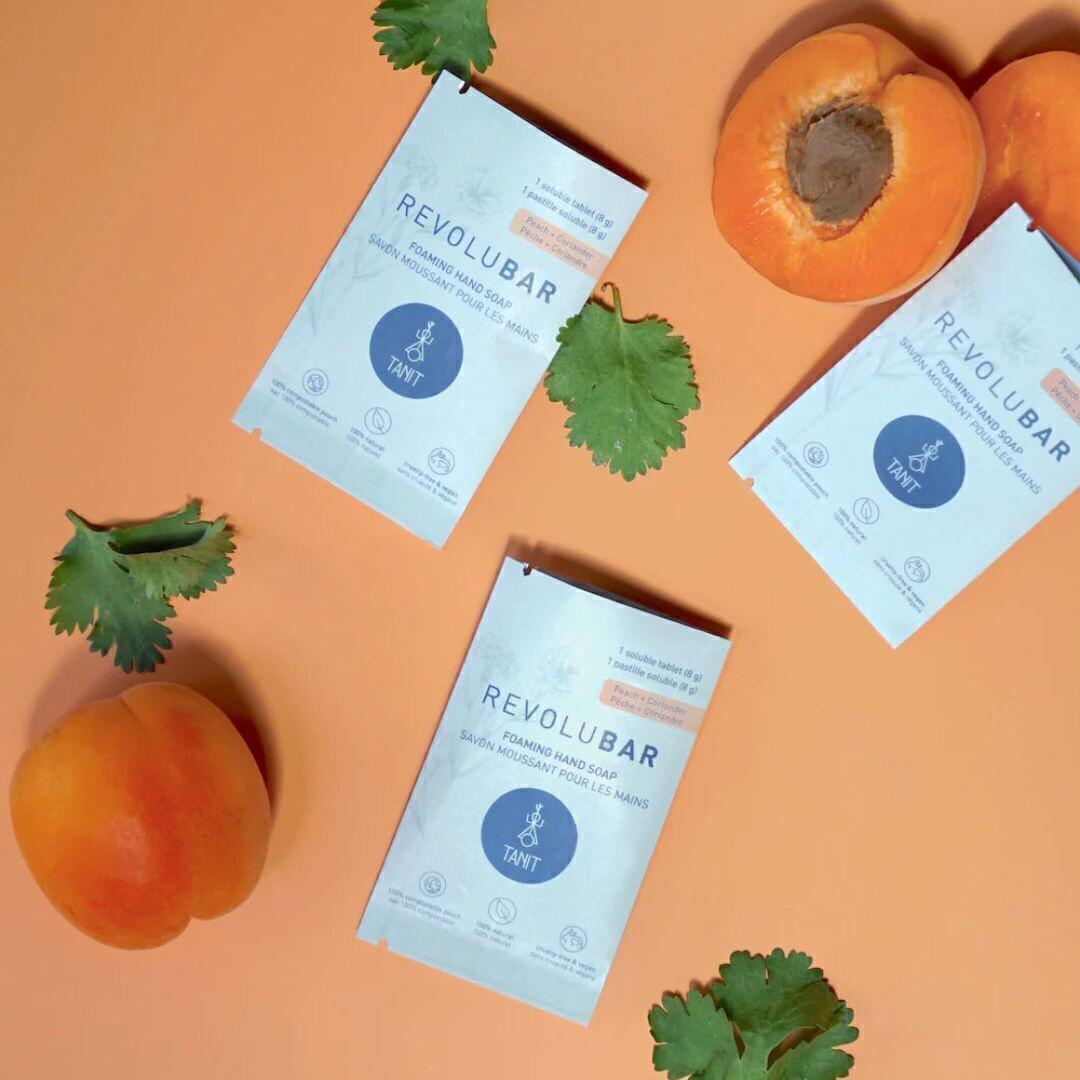 Tanit peach and coriander foaming hand soap tablets styled on an orange background with fresh apricot and herb leaves