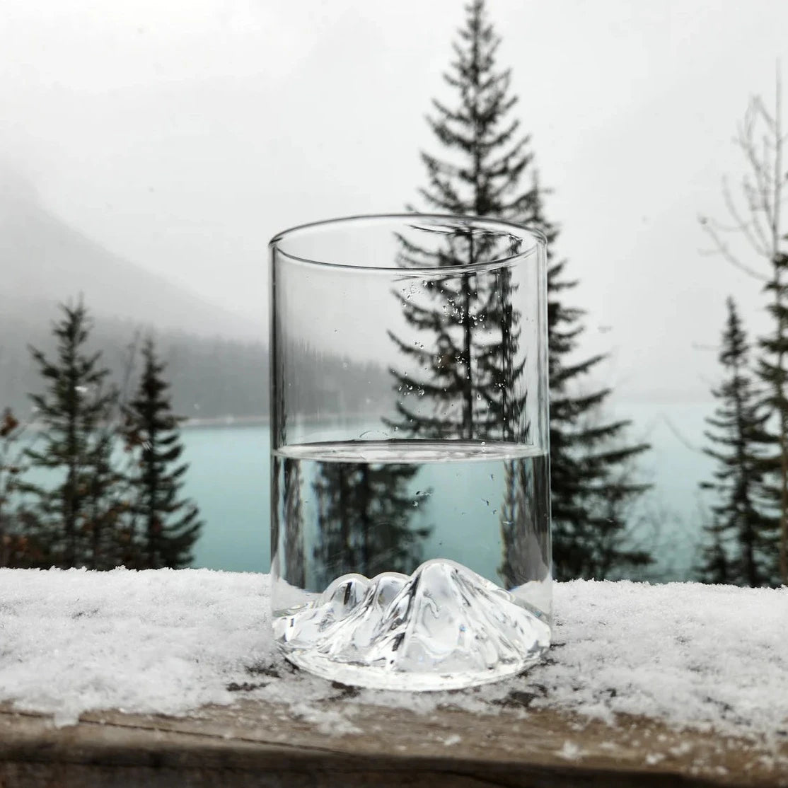 Three Sisters pint glass with 3D mountain detail, shown outdoors on snow-covered wood with trees and fog in background